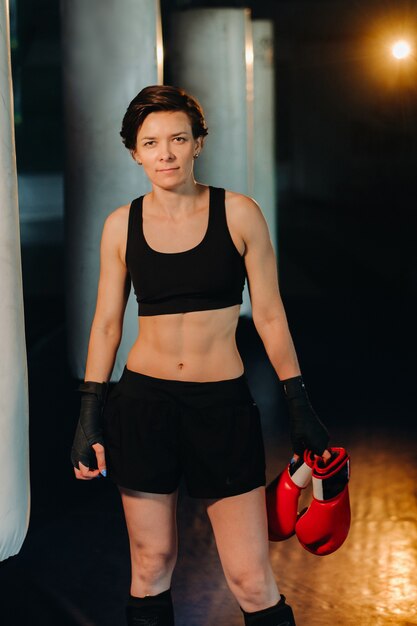 Портрет женщины-боксера в красных перчатках в тренажерном зале во время тренировки