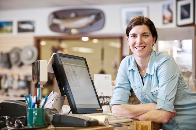 Portrait of a female caucasian owner next to the computer at the front desk of a flyfishing shop