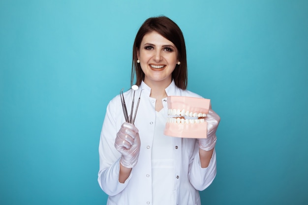 Portrait of female dentist holding medical stuff and fake jaw isolated.