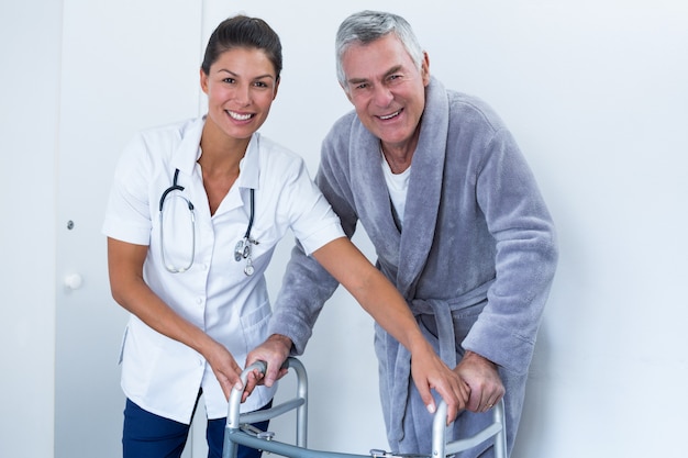 Portrait of female doctor helping senior man to walk with walker