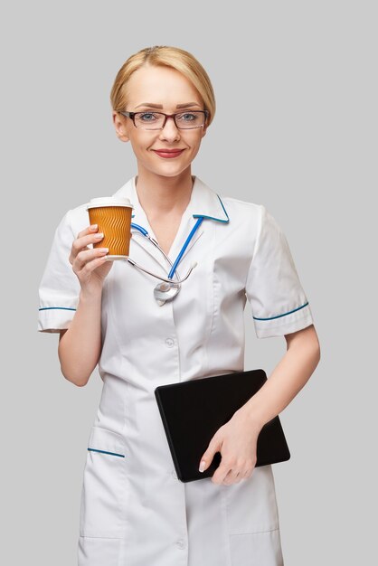 Portrait of a female doctor holding paper cup of coffee and holding tablet pc pad