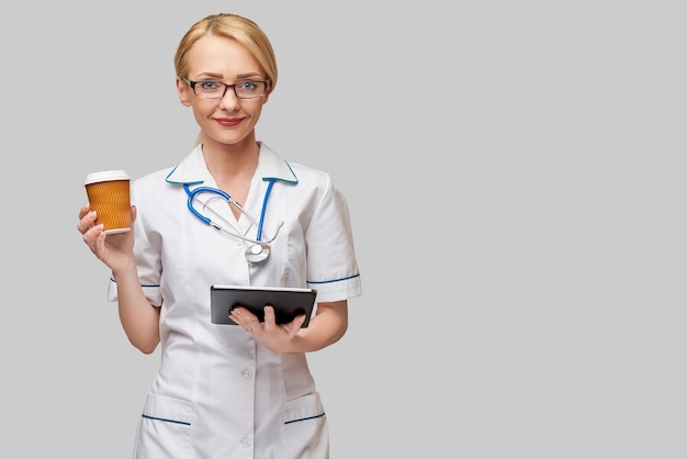 Portrait of a female doctor holding paper cup of coffee and holding tablet pc pad