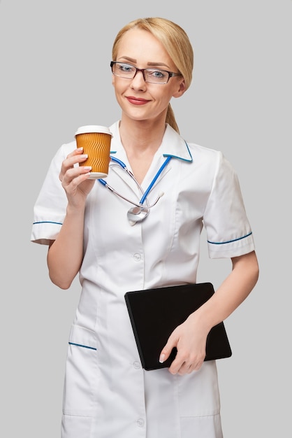 Portrait of a female doctor holding paper cup of coffee and holding tablet pc pad