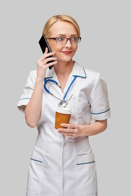 Portrait of a female doctor holding paper cup of coffee and talking on the phone