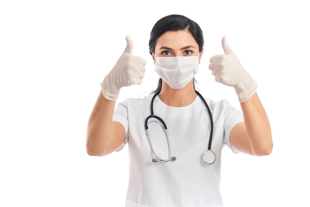 Portrait of female doctor wearing medical mask, glasses, and gloves showing thumbs up on white