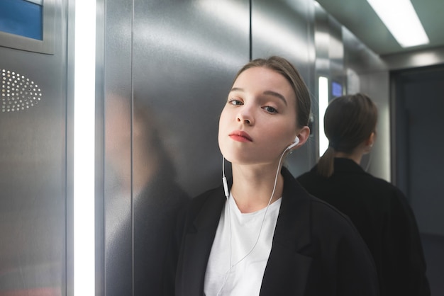 Portrait of a female employee in the elevator listening to music in her headphones.