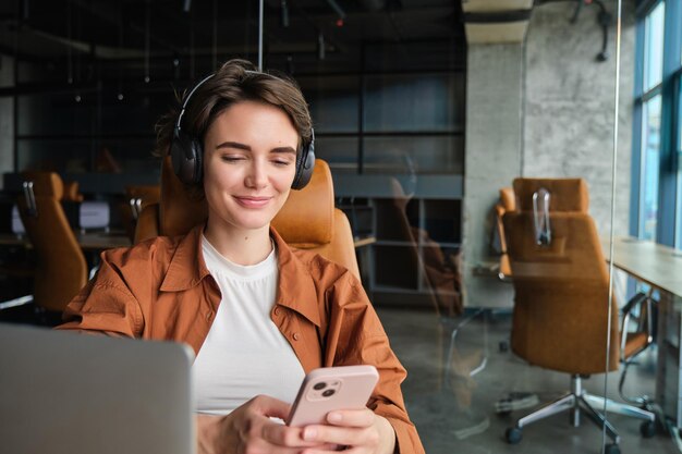 Portrait of female employee entrepreneur in office with laptop mobile phone wears wireless