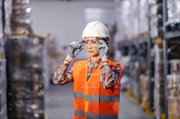 Photo portrait of a female factory worker is putting on protective glasses and preparing for work