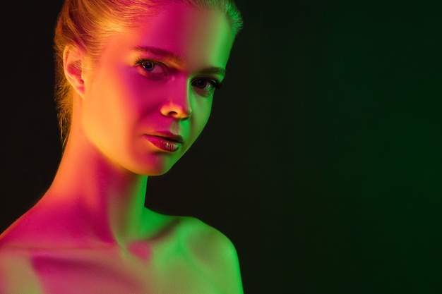 Portrait of female fashion model in neon light on dark studio background.