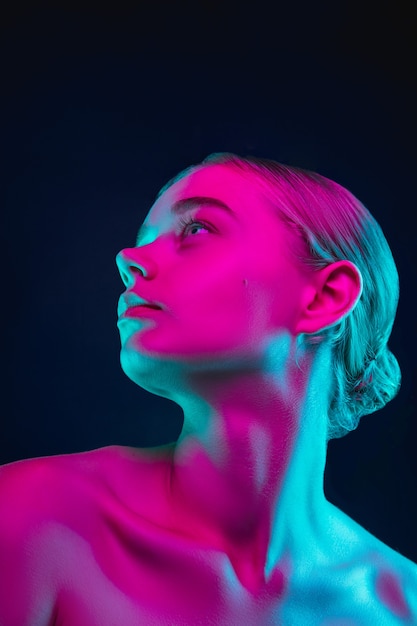 Portrait of female fashion model in neon light on dark studio background.