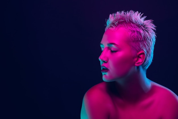 Portrait of female fashion model in neon light on dark studio background.