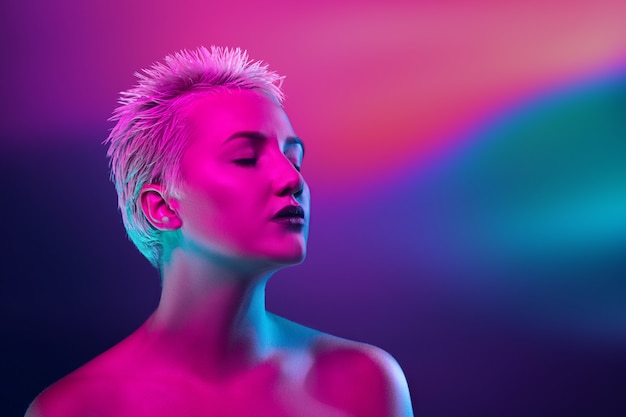Portrait of female fashion model in neon light on dark studio background