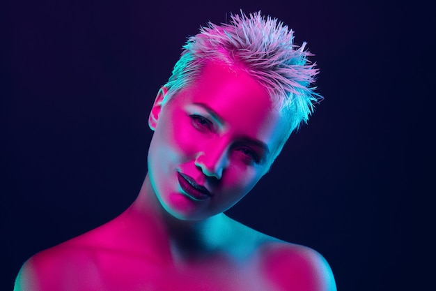 Portrait of female fashion model in neon light on dark studio background.