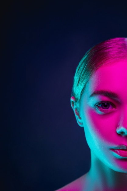 Photo portrait of female fashion model in neon light on dark studio background.