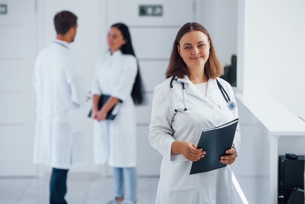 Portrait of female foctor stands in the hospital with employees behind.