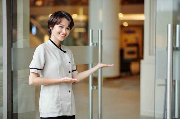 Portrait of female hotel worker inviting guests inside fancy hotel