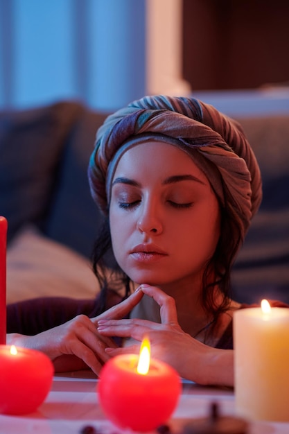 Portrait of a female leaning on the divination desk with burning candles during the meditation