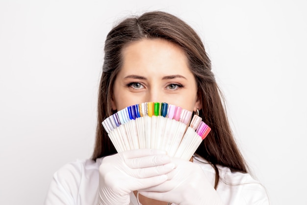 Portrait of female manicure master covering her face with nail sample palette