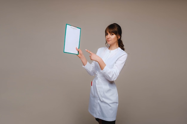 Portrait of a female medical worker in a gray background with a medical report.Girl doctor with a Notepad