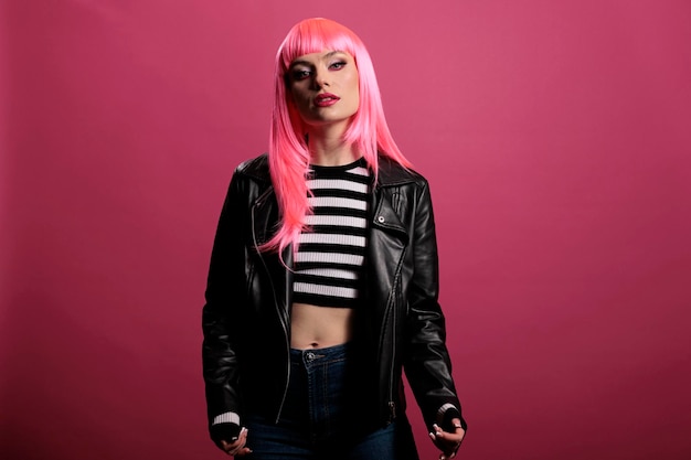 스튜디오에서 세련된 가죽 재킷을 입은 여성 모델의 초상화, 펑크 로커 스타일로 평온하고 관능적인 느낌. 분홍색 머리를 하고 펑키하고 배경 위에 놀라운 패션을 매혹시킵니다.