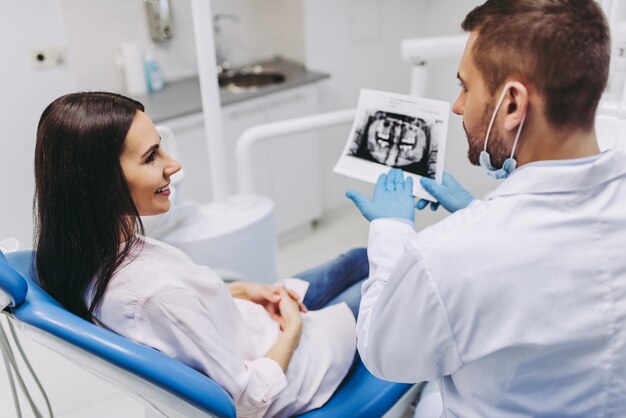 Portrait of female patient talking with male dentist looking at xray in modern clinic