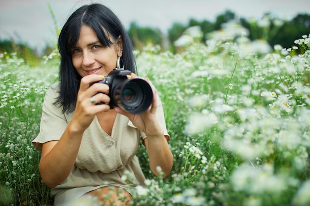 Il ritratto del fotografo femminile prende la foto all'aperto sul paesaggio del campo di fiori che tiene una macchina fotografica, la donna tiene la macchina fotografica digitale nelle sue mani. fotografia naturalistica di viaggio, spazio per il testo, vista dall'alto.