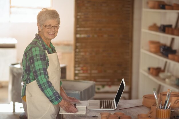 Photo portrait of female potter making note from laptop