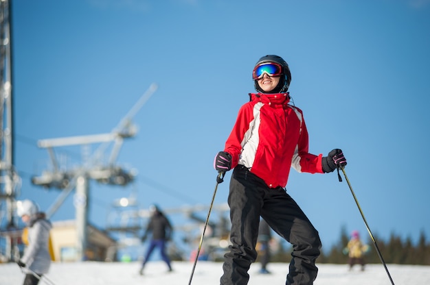 Portrait of female skier standing with skis on mountain top at a winter resort in sunny day