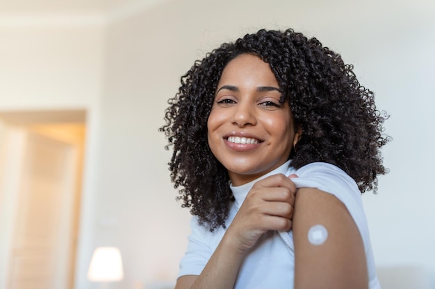 Портрет женщины, улыбающейся после вакцинации Женщина держит рукав рубашки и показывает руку с повязкой после вакцинации