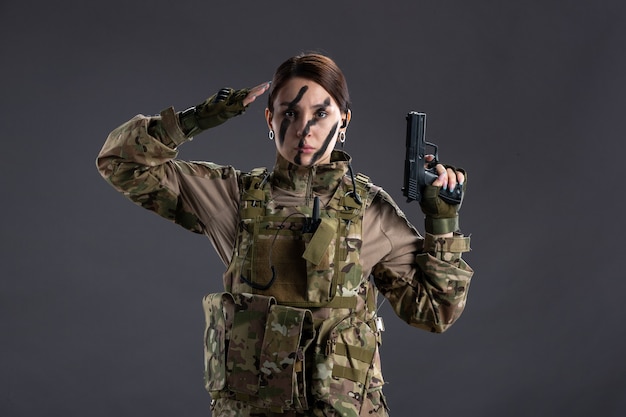 Portrait of female soldier in camouflage with gun on dark wall