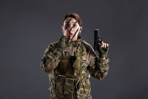 Photo portrait of female soldier in camouflage with gun dark wall