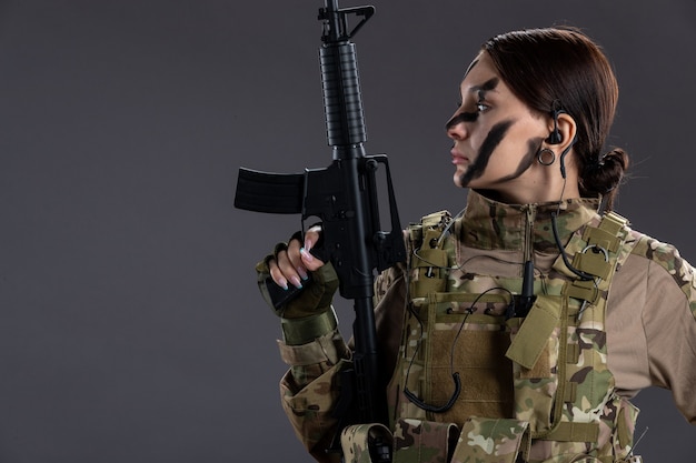 Portrait of female soldier in military uniform with machine gun on dark wall