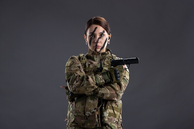 Portrait of female soldier with gun in camouflage dark wall