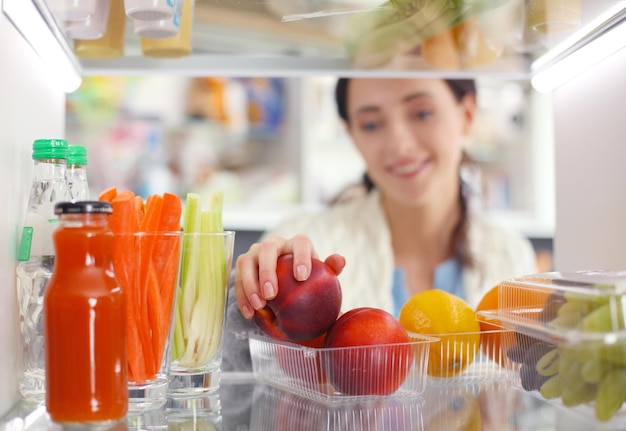 健康食品の野菜や果物でいっぱいの開いた冷蔵庫の近くに立っている女性の肖像画