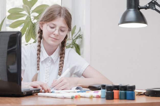 Portrait of female student enjoying learning in coworking office using laptop computer for research, freelancer during making project for remote job making notes. Pupil concentrated drawing notes