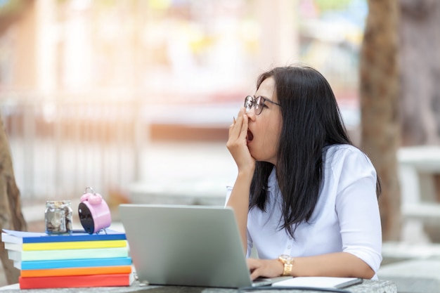 Ritratto della studentessa che si siede al parco e che per mezzo del computer portatile