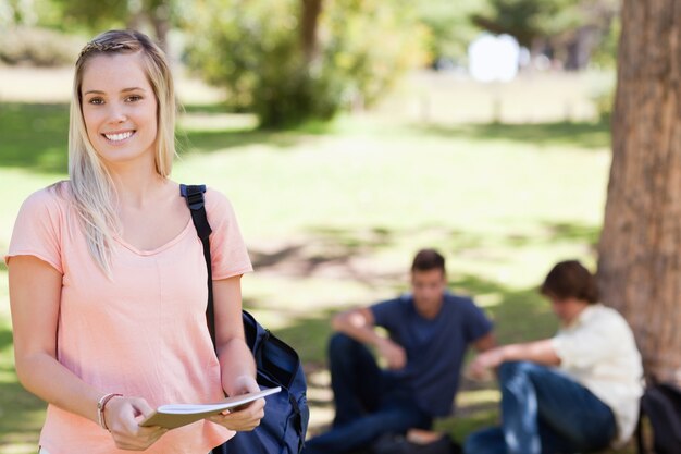 教科書を持っている間に笑っている女性学生の肖像