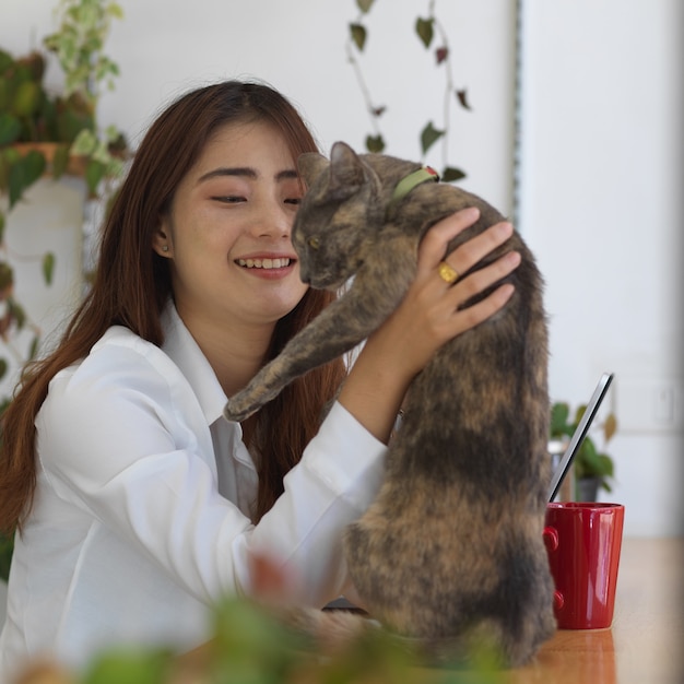 Portrait of female teenager playing with her cat while relaxing with digital tablet in living room