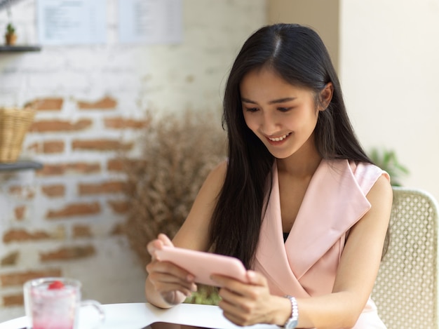 Портрет девушки-подростка, расслабляющейся со смартфоном и напитком на журнальном столике в кафе
