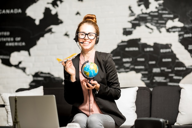 Ritratto di un'agente di viaggio femminile in tuta e auricolare che gioca con il globo e l'aeroplano sullo sfondo della mappa del mondo