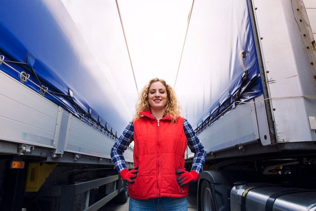 Foto ritratto di donna camionista orgogliosamente in piedi tra rimorchi e camion.