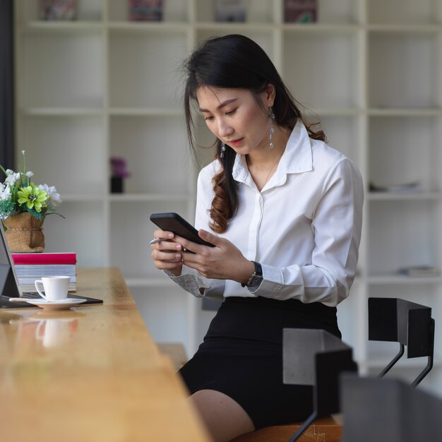 Portrait of female university student relaxing with smartphone while doing assignment in cafe