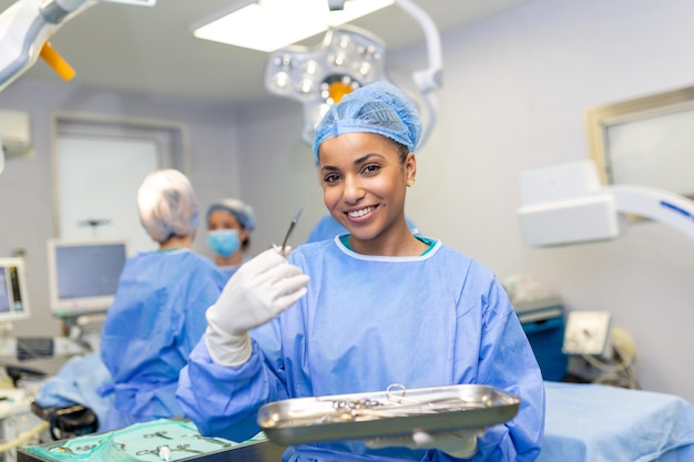 Portrait of female woman nurse surgeon OR staff member dressed in surgical scrubs gown mask and hair net in hospital operating room theater making eye contact smiling pleased happy looking at camera