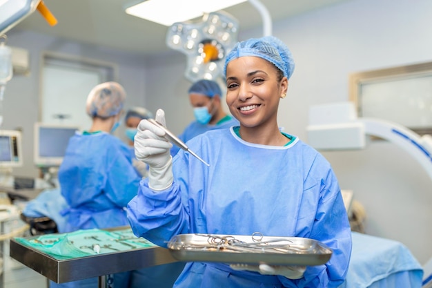 Portrait of female woman nurse surgeon or staff member dressed\
in surgical scrubs gown mask and hair net in hospital operating\
room theater making eye contact smiling pleased happy looking at\
camera