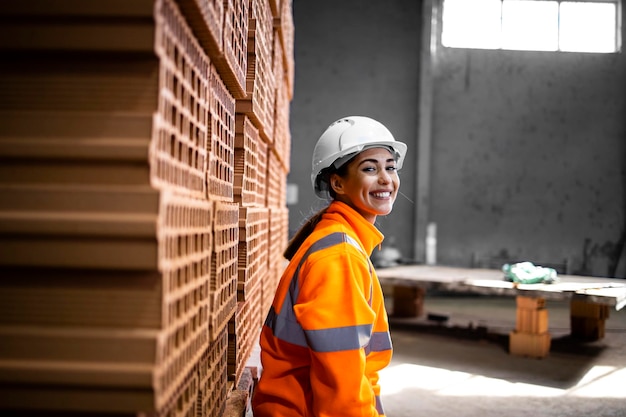 Ritratto di lavoratrice in abiti ad alta visibilità e elmetto che lavora nella fabbrica di produzione