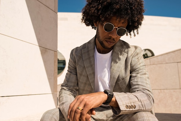 Portrait of fine-looking African American man outdoors. Man in suit with beard sitting at terrace or rooftops. Checking time.  Portrait, city life concept