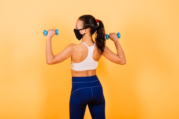 Portrait of fit african woman wearing face mask. Sporty woman in fitness wear standing on a yellow background.