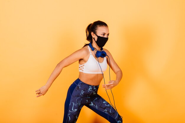 Ritratto di fit donna africana che indossa la maschera per il viso. donna sportiva in abbigliamento fitness in piedi su uno sfondo giallo.