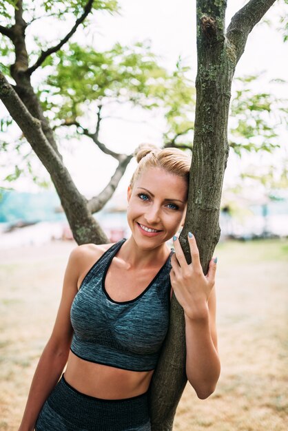 Portrait of fit blonde woman leaning on a tree.