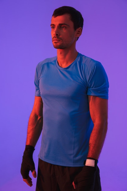 Portrait of a fit confident sportsman doing boxing exercises isolated over violet wall